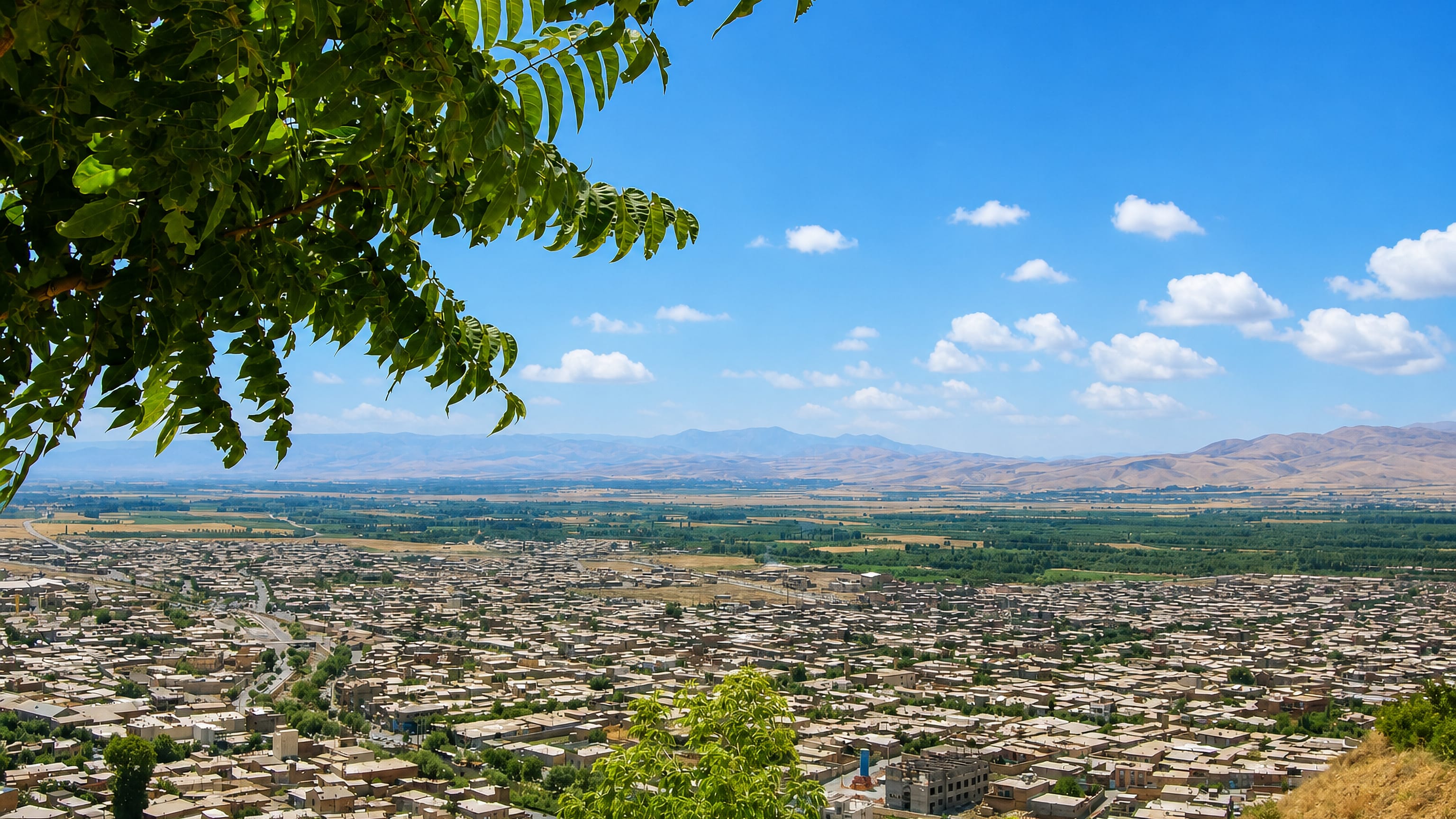Hillside view over Oshnavīyeh, Iran, its flat-roofed houses spread across a valley below bare mountains.