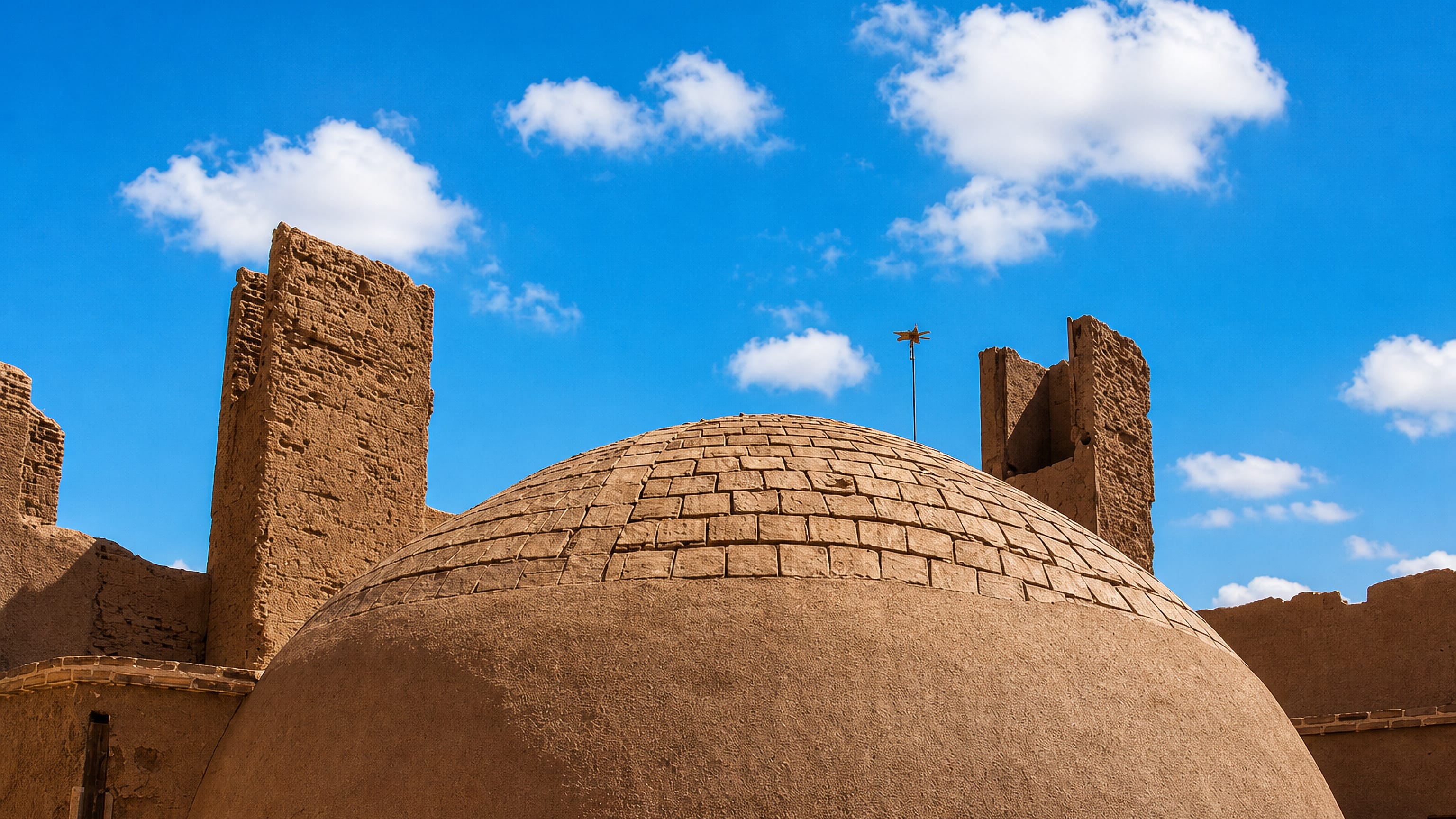 Adobe dome and mud-brick windcatcher walls under a blue sky in Ardakan, Yazd province, Iran.