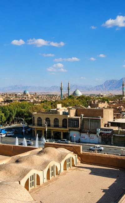 Rooftops, windcatchers, domes and minarets of the mudbrick old city of Yazd with mountains beyond.