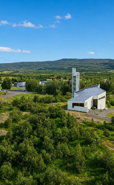 Egilsstaðir's white church with its slender bell tower among low buildings in a green East Iceland valley under blue sky