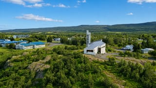 Egilsstaðir's white church with its slender bell tower among low buildings in a green East Iceland valley under blue sky