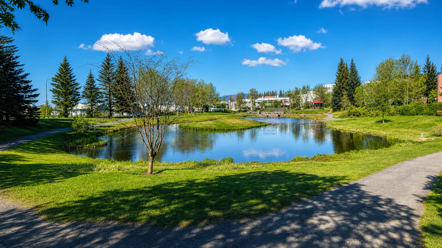 Grassy park with a still pond and low-rise housing beyond in Breiðholt, a suburb of Reykjavík, Iceland.