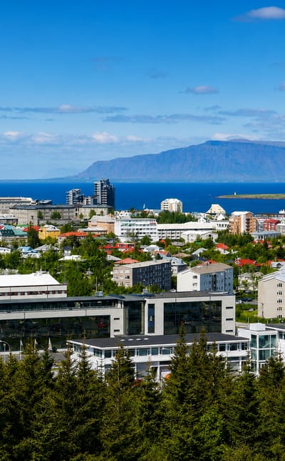 Elevated view over Reykjavík's Hlíðar district toward Hallgrímskirkja, the bay and Mount Esja under a blue sky