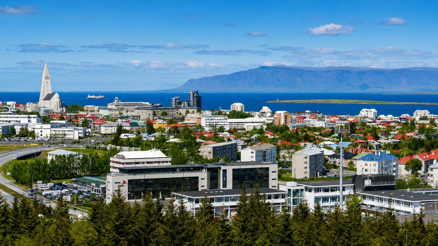 Elevated view over Reykjavík's Hlíðar district toward Hallgrímskirkja, the bay and Mount Esja under a blue sky