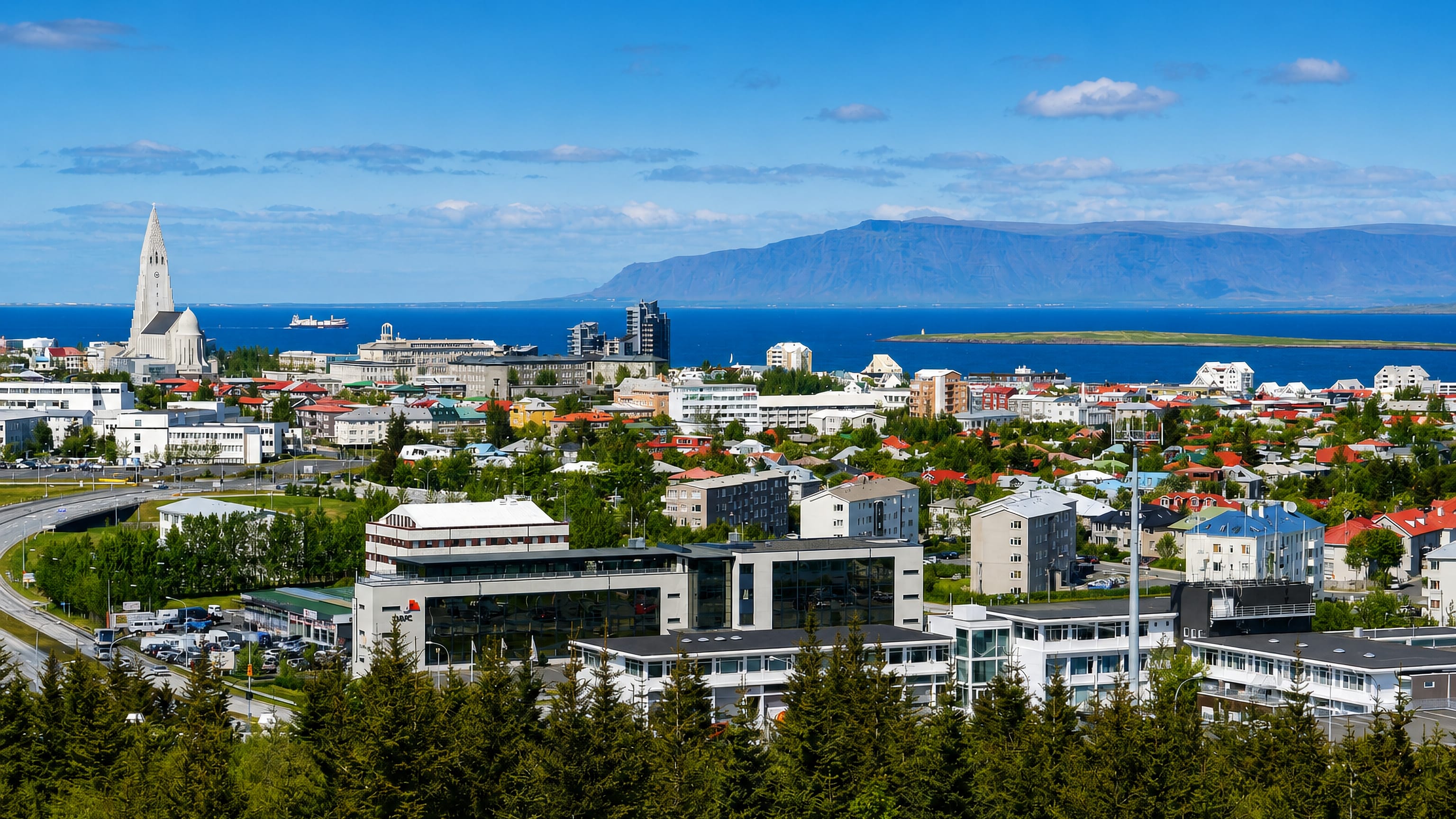 Elevated view over Reykjavík's Hlíðar district toward Hallgrímskirkja, the bay and Mount Esja under a blue sky