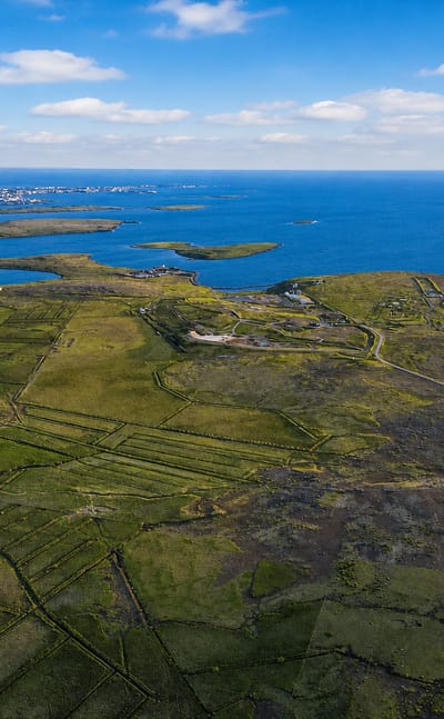 Aerial view of the green Kjalarnes peninsula and coastline north of Reykjavik with the city skyline on the horizon