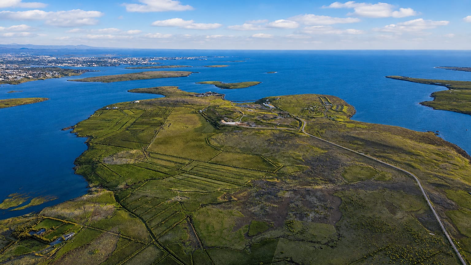 Aerial view of the green Kjalarnes peninsula and coastline north of Reykjavik with the city skyline on the horizon