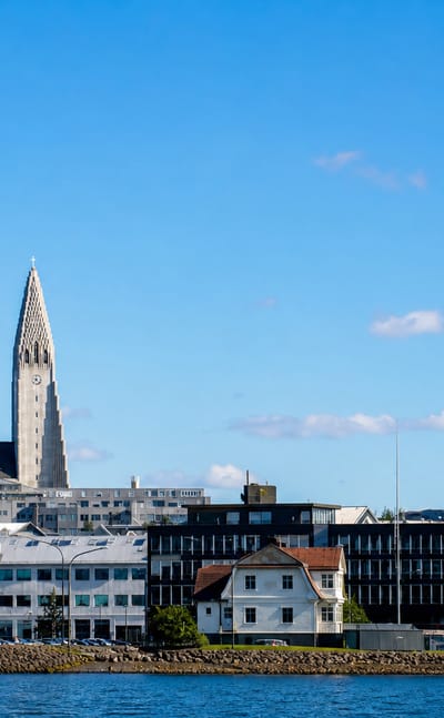 Waterfront view of Reykjavík's Miðborg district with a tall church spire rising above colourful buildings under a blue sky.