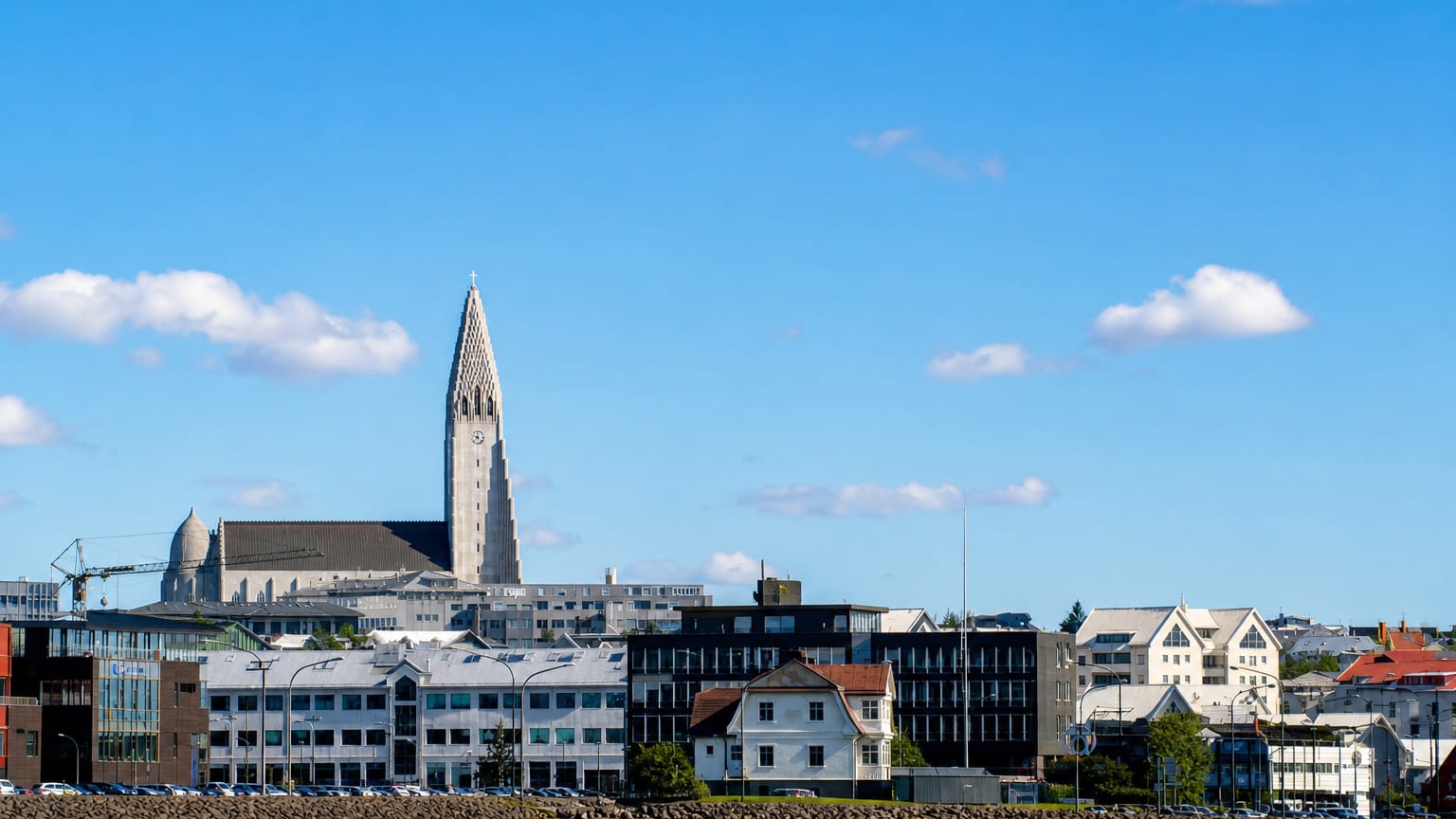 Waterfront view of Reykjavík's Miðborg district with a tall church spire rising above colourful buildings under a blue sky.