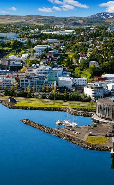 Aerial view of Akureyri, Iceland, a colorful fjord-side town and harbor below green mountains by Eyjafjörður.