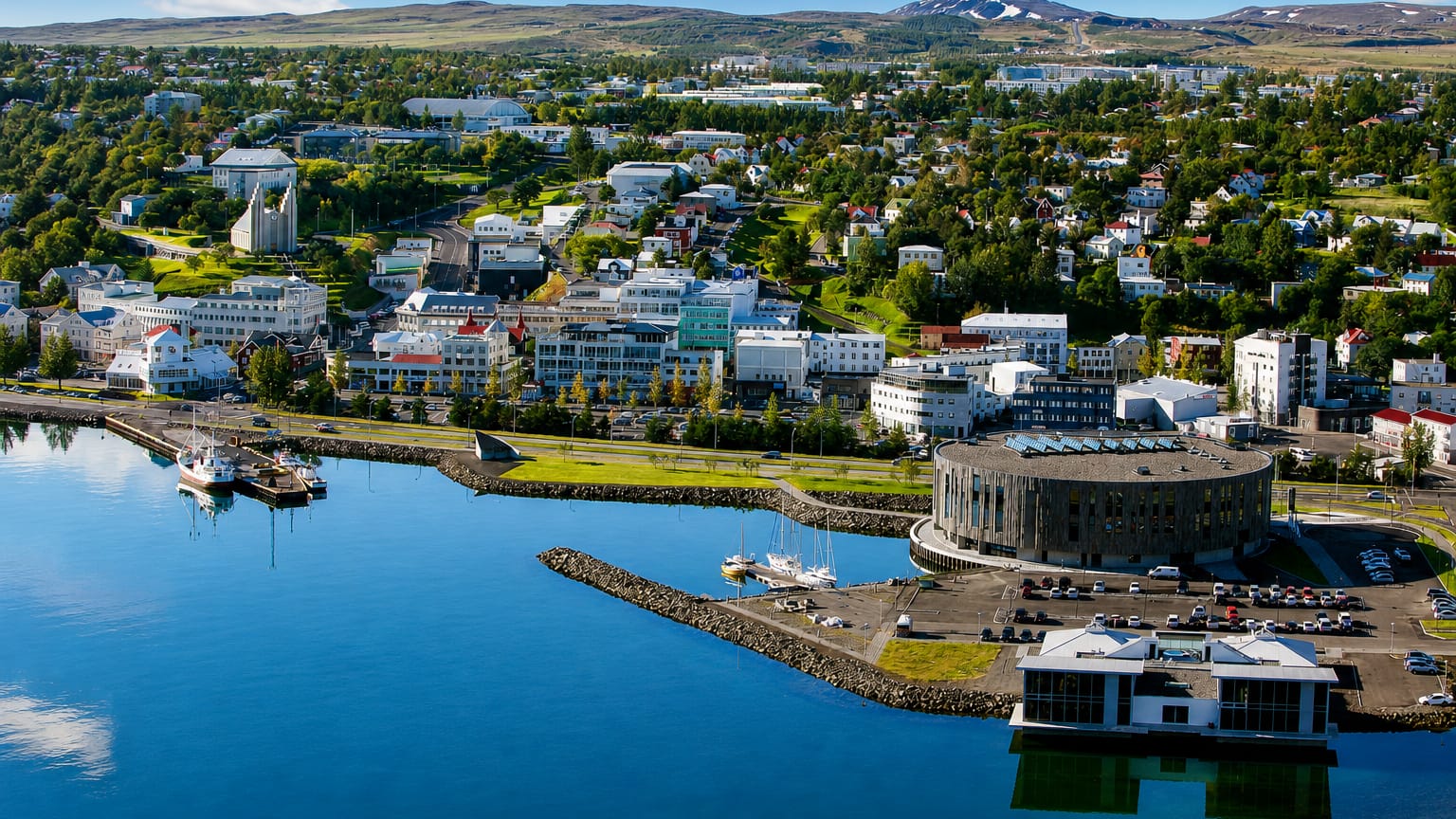 Aerial view of Akureyri, Iceland, a colorful fjord-side town and harbor below green mountains by Eyjafjörður.