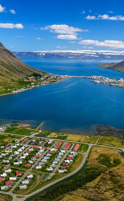 Ísafjörður's spit-shaped town reaching into Skutulsfjörður fjord, ringed by steep flat-topped Westfjords mountains and snow patches.
