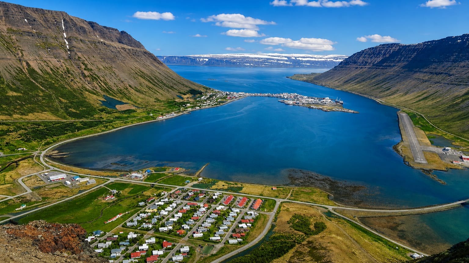 Ísafjörður's spit-shaped town reaching into Skutulsfjörður fjord, ringed by steep flat-topped Westfjords mountains and snow patches.