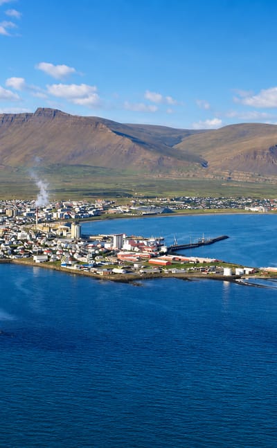 Aerial view of Akranes, Iceland, a peninsula town with a lighthouse beneath the twin-peaked Akrafjall mountain.
