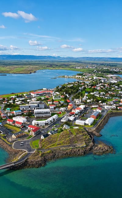 Aerial view of Borgarnes, Iceland, a colorful town on a peninsula ringed by turquoise sea with a causeway and distant mountains
