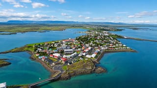Aerial view of Borgarnes, Iceland, a colorful town on a peninsula ringed by turquoise sea with a causeway and distant mountains