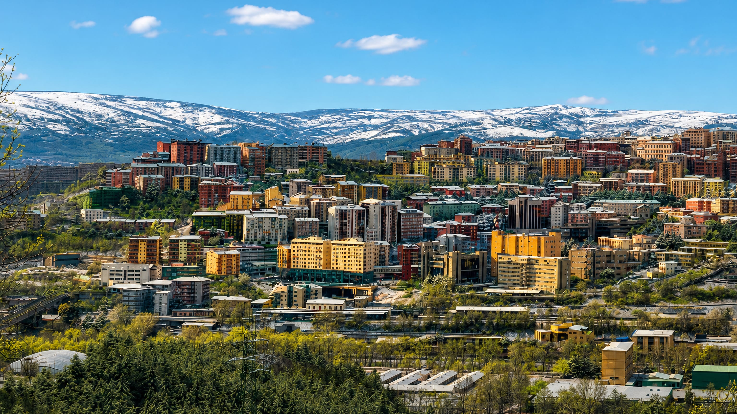 Potenza's ridge of colourful apartment blocks in Basilicata, backed by snow-capped Apennine mountains under blue sky.