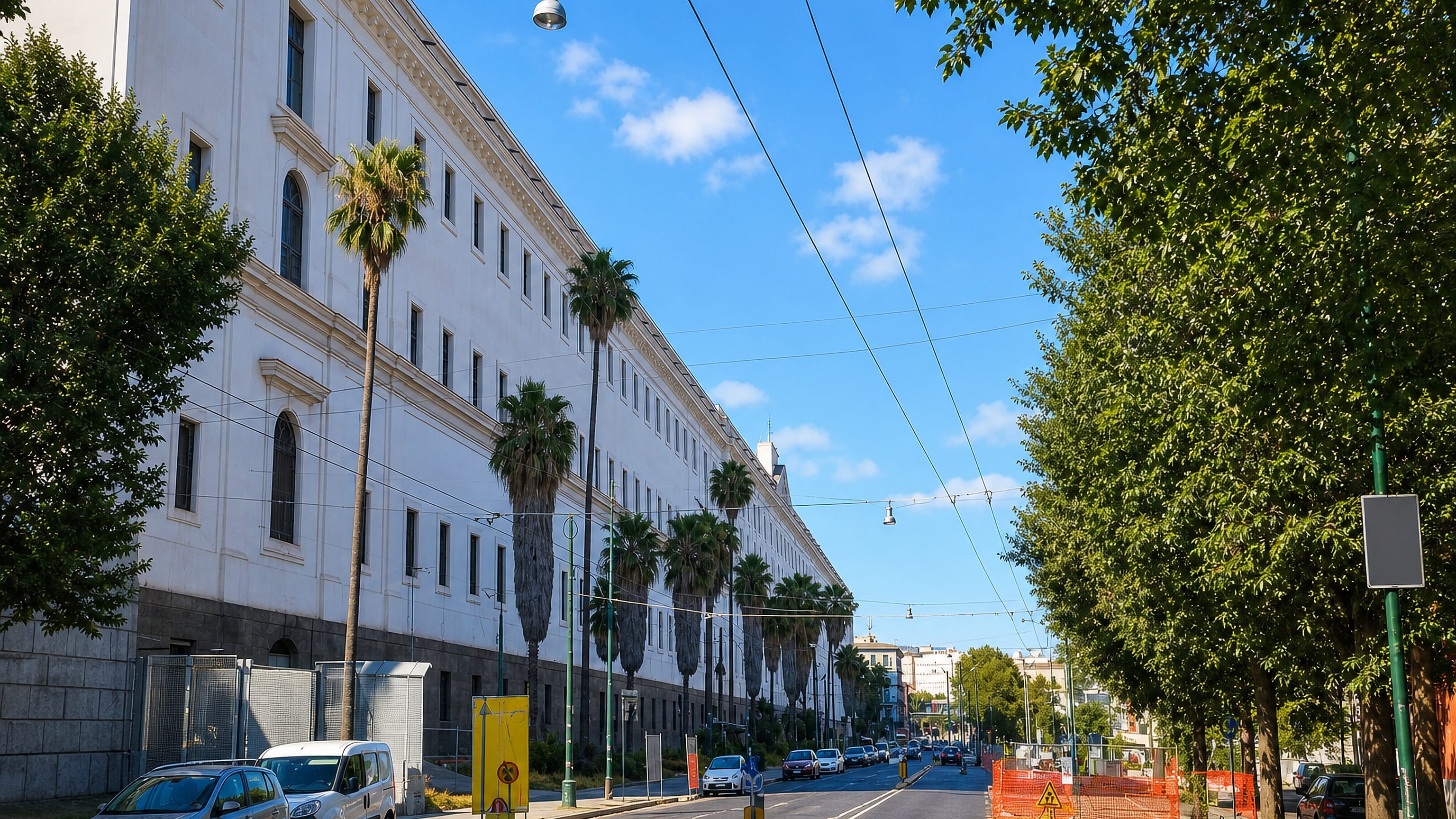 Palm-lined boulevard beside a long neoclassical facade in Naples' San Carlo all'Arena district.