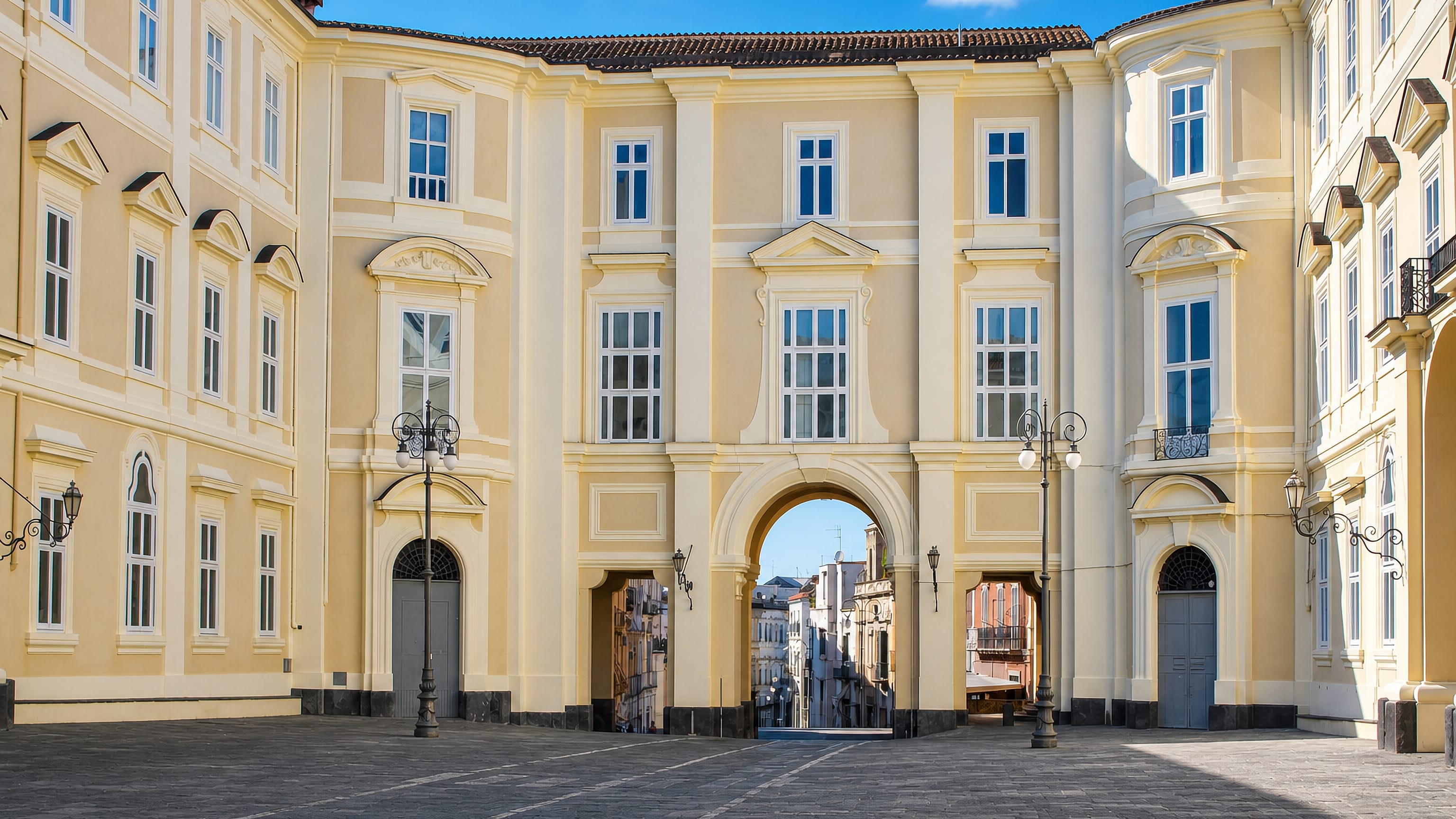 The pale-yellow Baroque courtyard of the Royal Palace of Portici, its arch opening onto the town street.