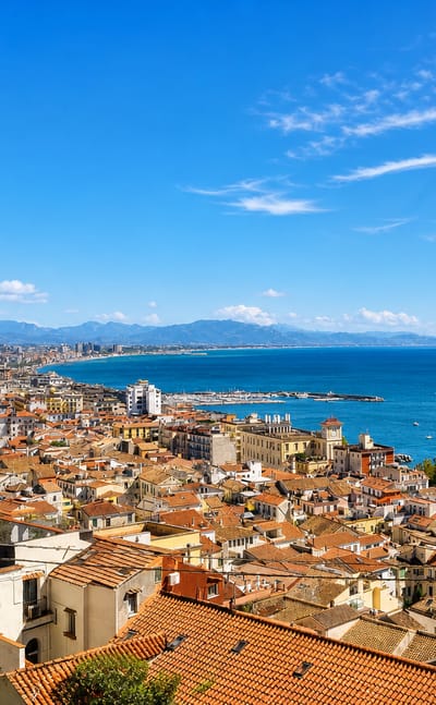 Terracotta rooftops of Salerno descending to the Gulf of Salerno with coastal mountains under a clear sky