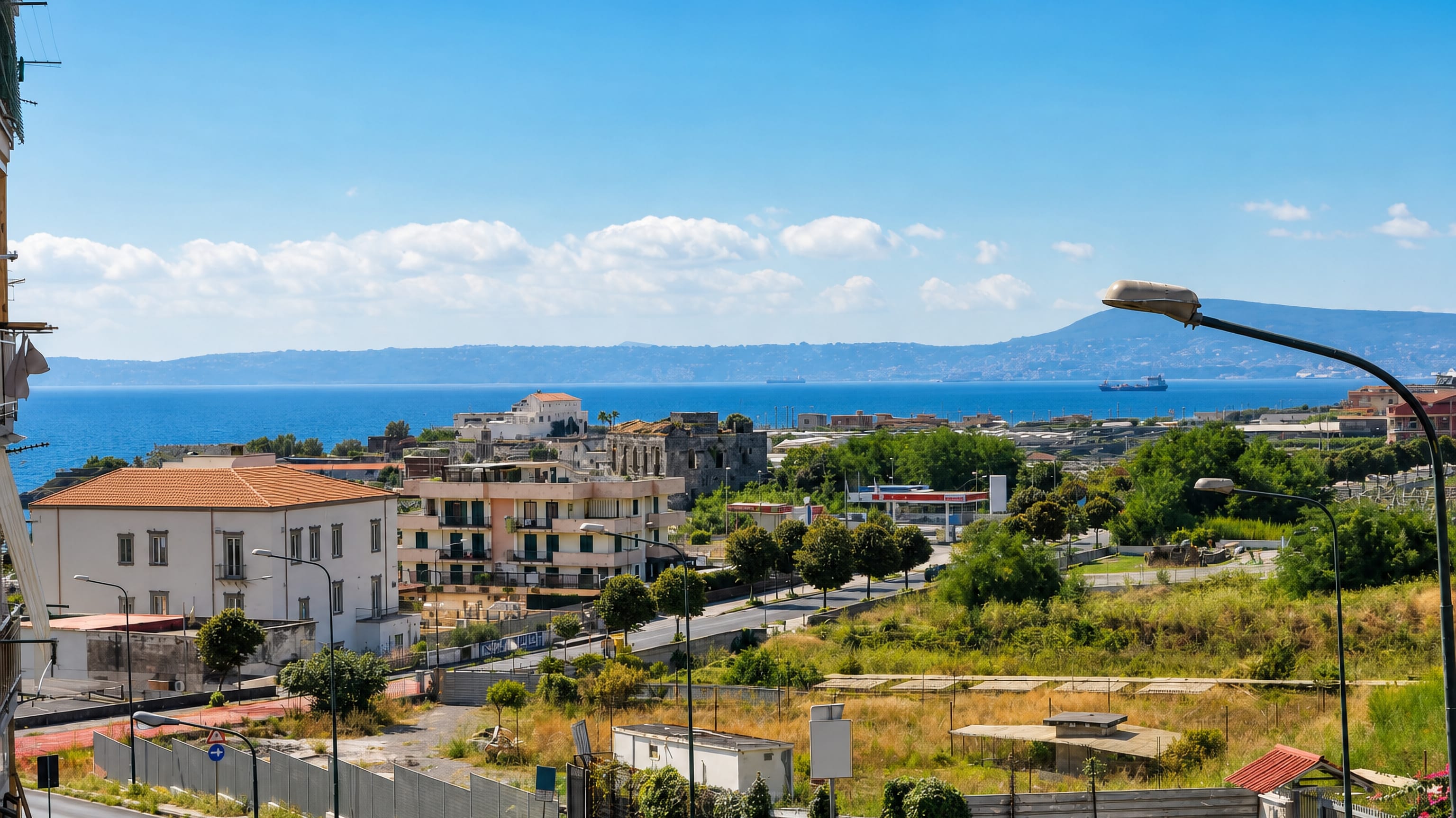 Hillside view over Torre del Greco rooftops to the Bay of Naples with cargo ships and distant headlands.