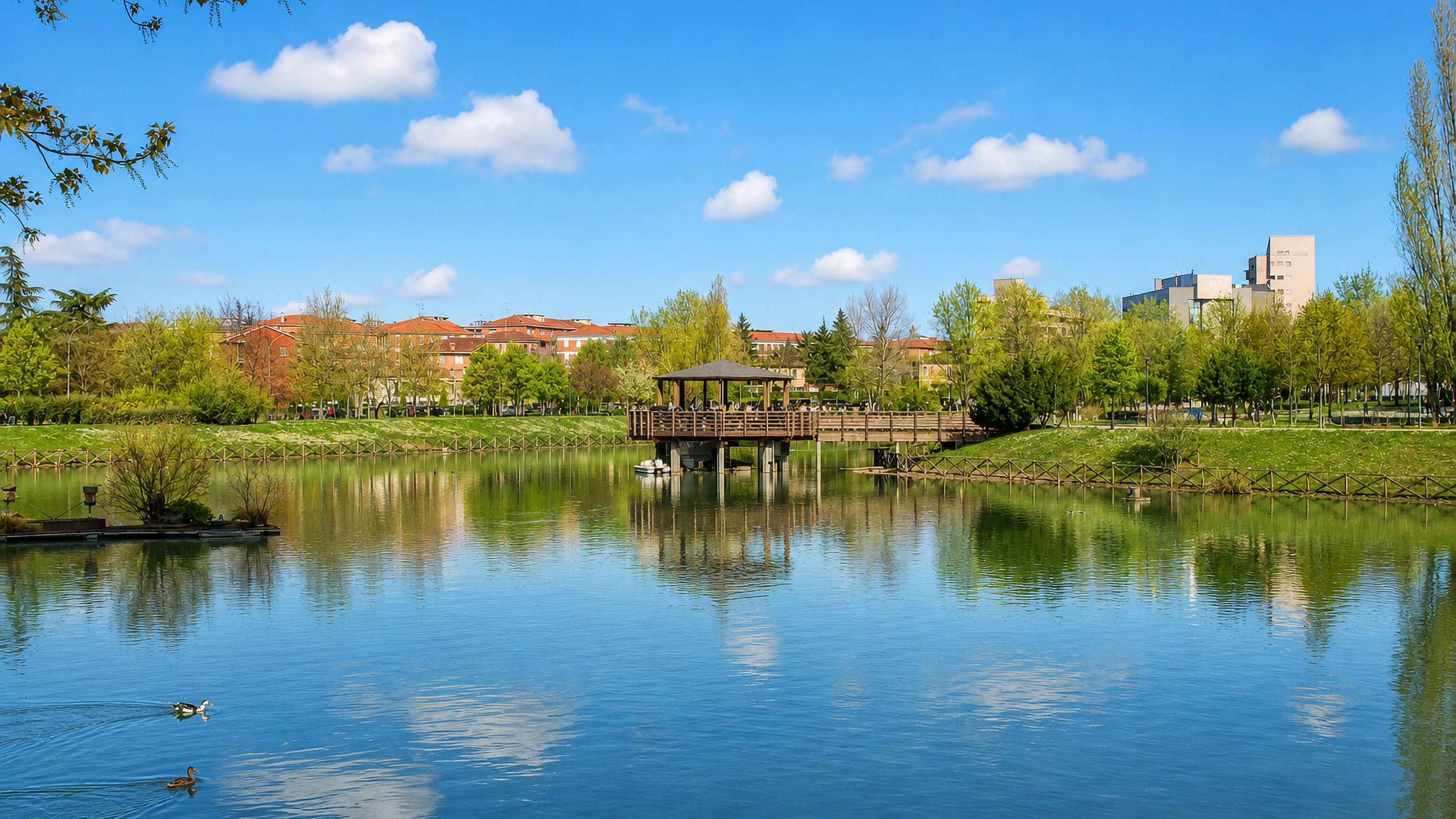 Park lake with a wooden gazebo and ducks backed by housing in Corticella, northern Bologna
