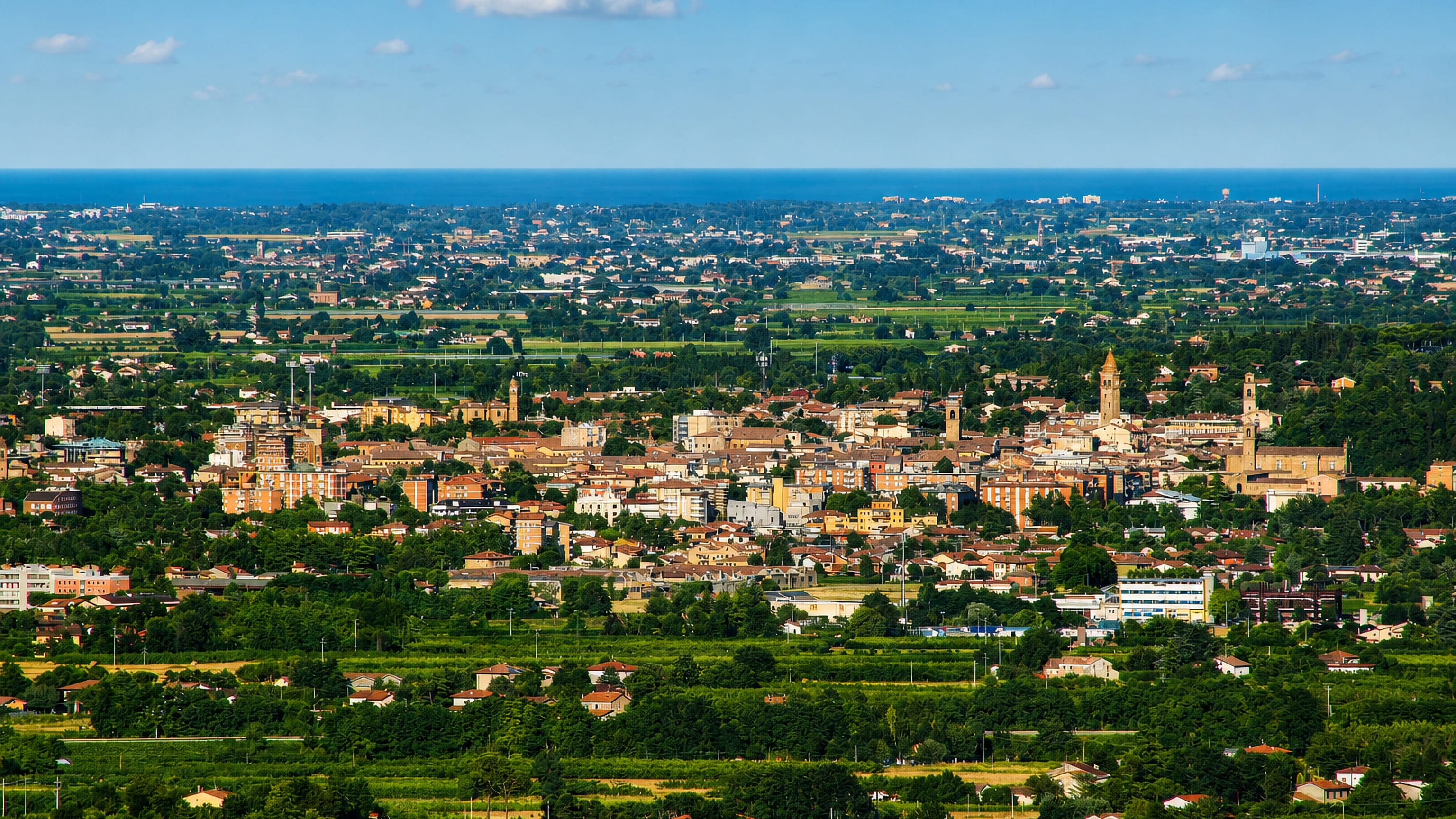 Terracotta rooftops and bell towers of Cesena spread across the Romagna plain toward the Adriatic.