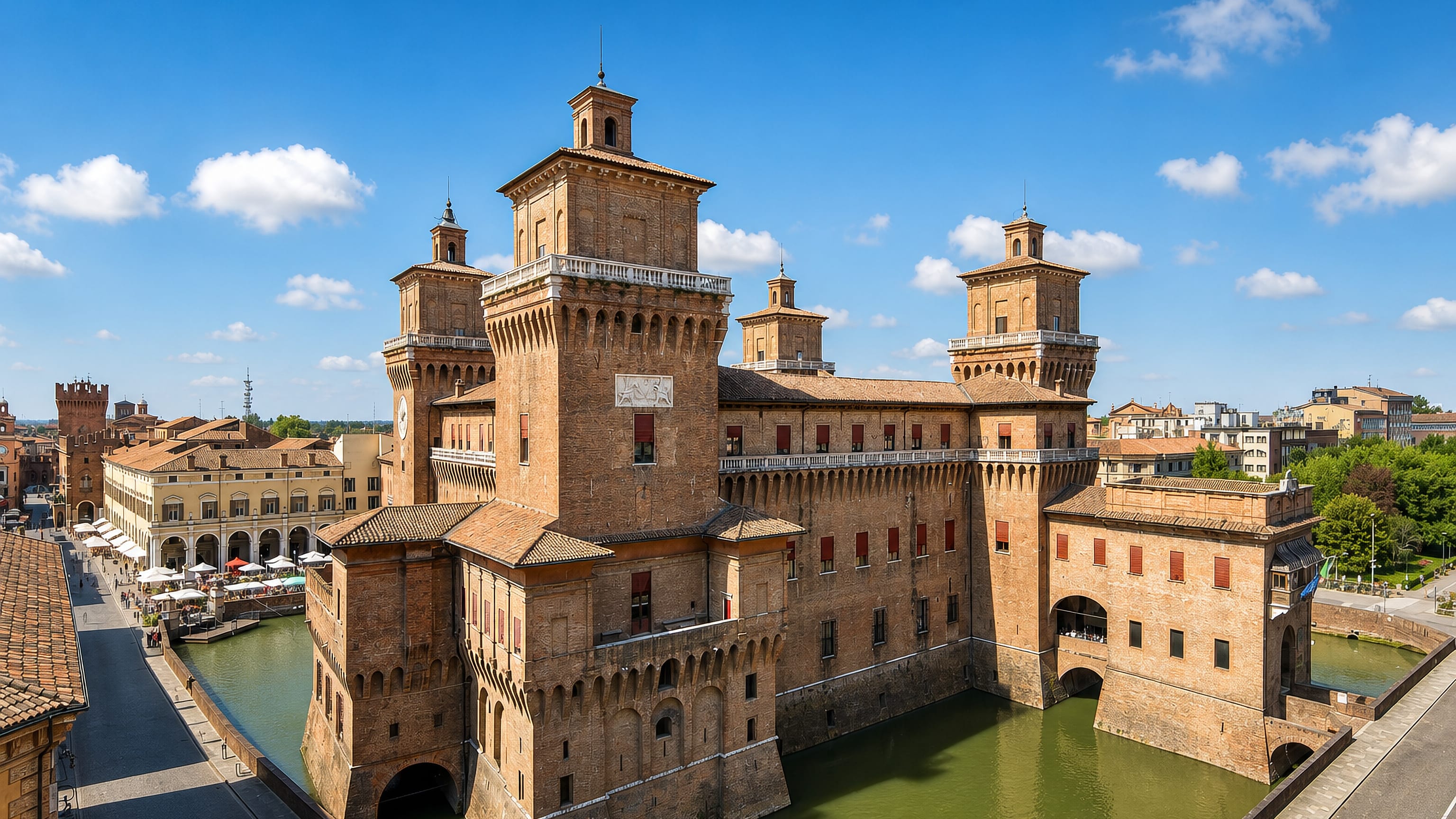 Castello Estense's brick towers and water-filled moat rising over Ferrara's old town under a blue sky.