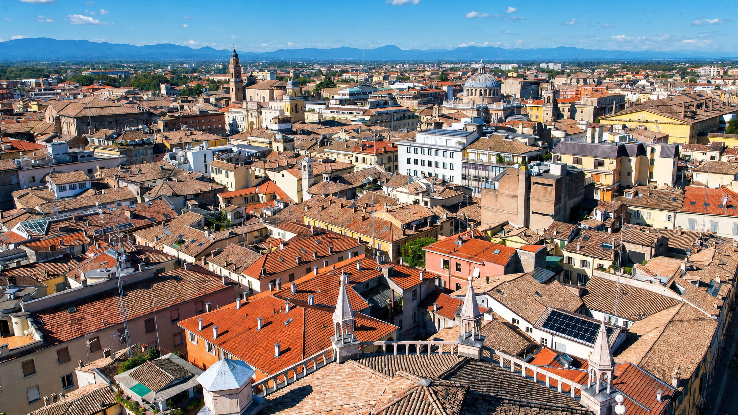 Parma's terracotta rooftops from above, with Baptistery spires in the foreground and church domes beyond