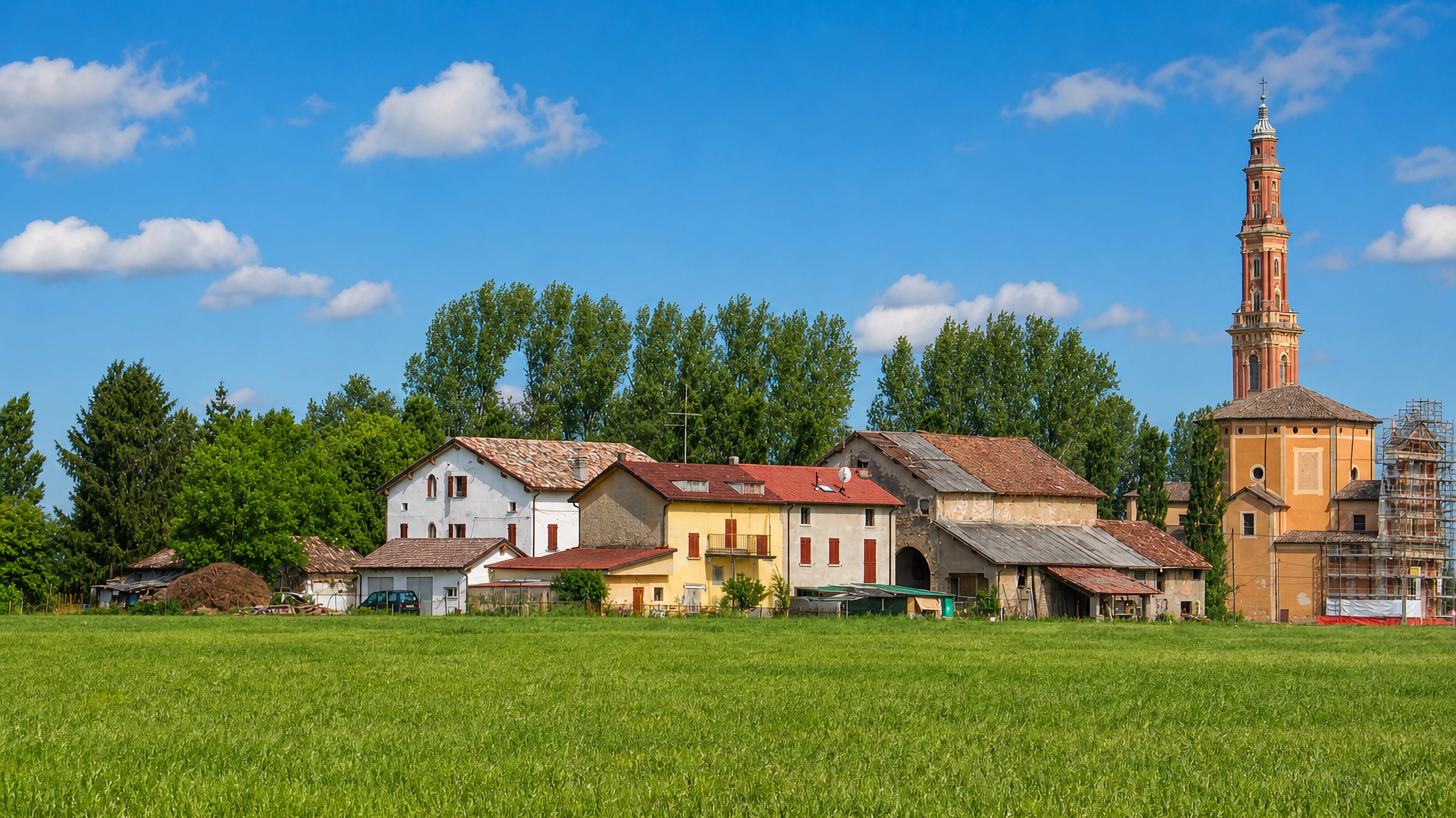 Farmhouses and a tall brick bell tower rising over green fields at Sesso, near Reggio nell'Emilia.