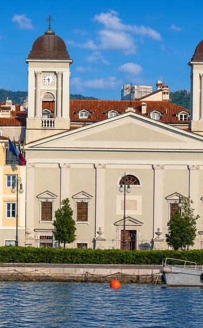 Trieste waterfront with the twin-towered Greek Orthodox Church of San Nicolò and boats moored on the Adriatic.
