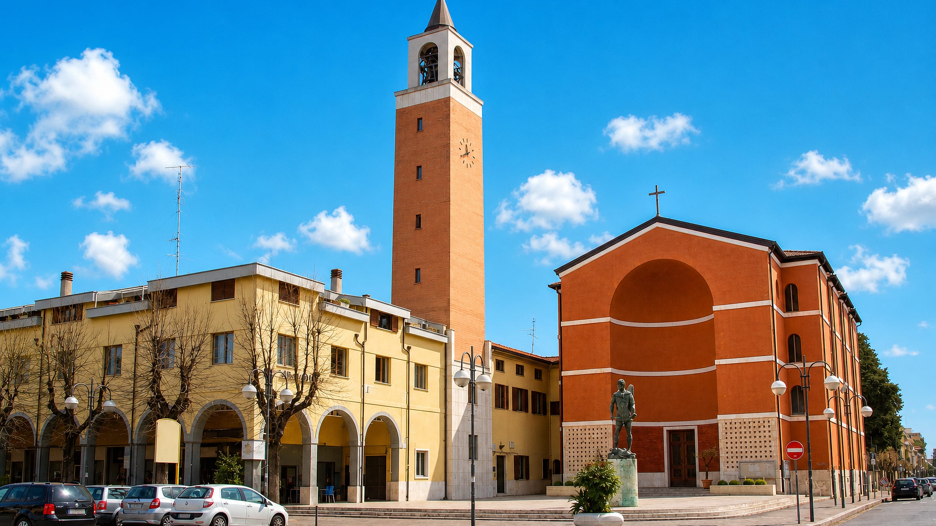 Aprilia's central piazza with the brick campanile of San Michele Arcangelo and its arcaded 1930s blocks.