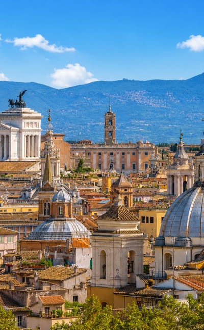 Rome skyline with the Altare della Patria monument, church domes and rooftops backed by hills under a blue sky