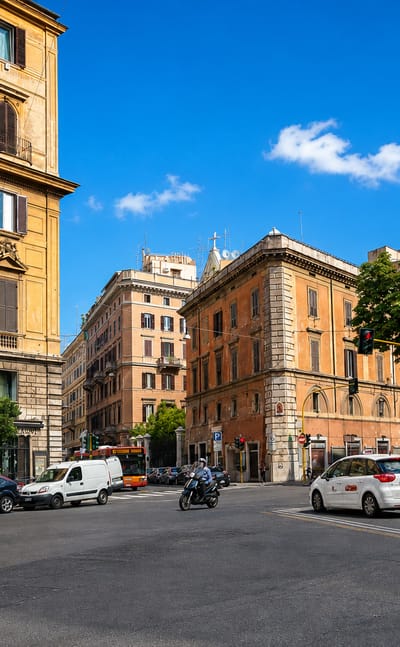 Sunlit street corner in Rome with ochre palazzi, parked cars and a clear blue sky in the Castro Pretorio quarter