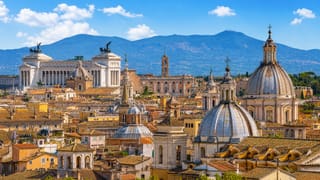 Rome skyline with the Altare della Patria monument, church domes and rooftops backed by hills under a blue sky