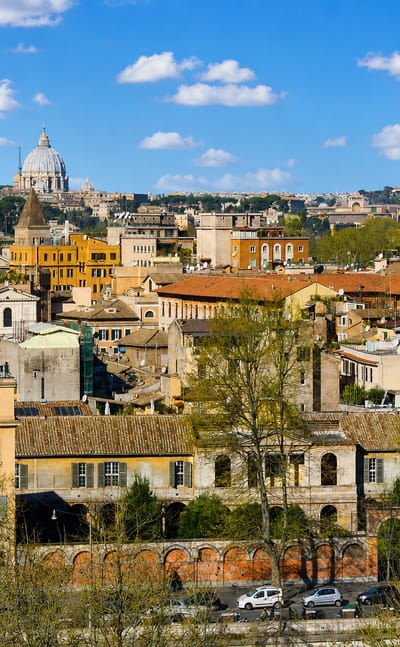 Trastevere's terracotta rooftops and a Romanesque bell tower in Rome below the dome of St. Peter's Basilica under a blue sky