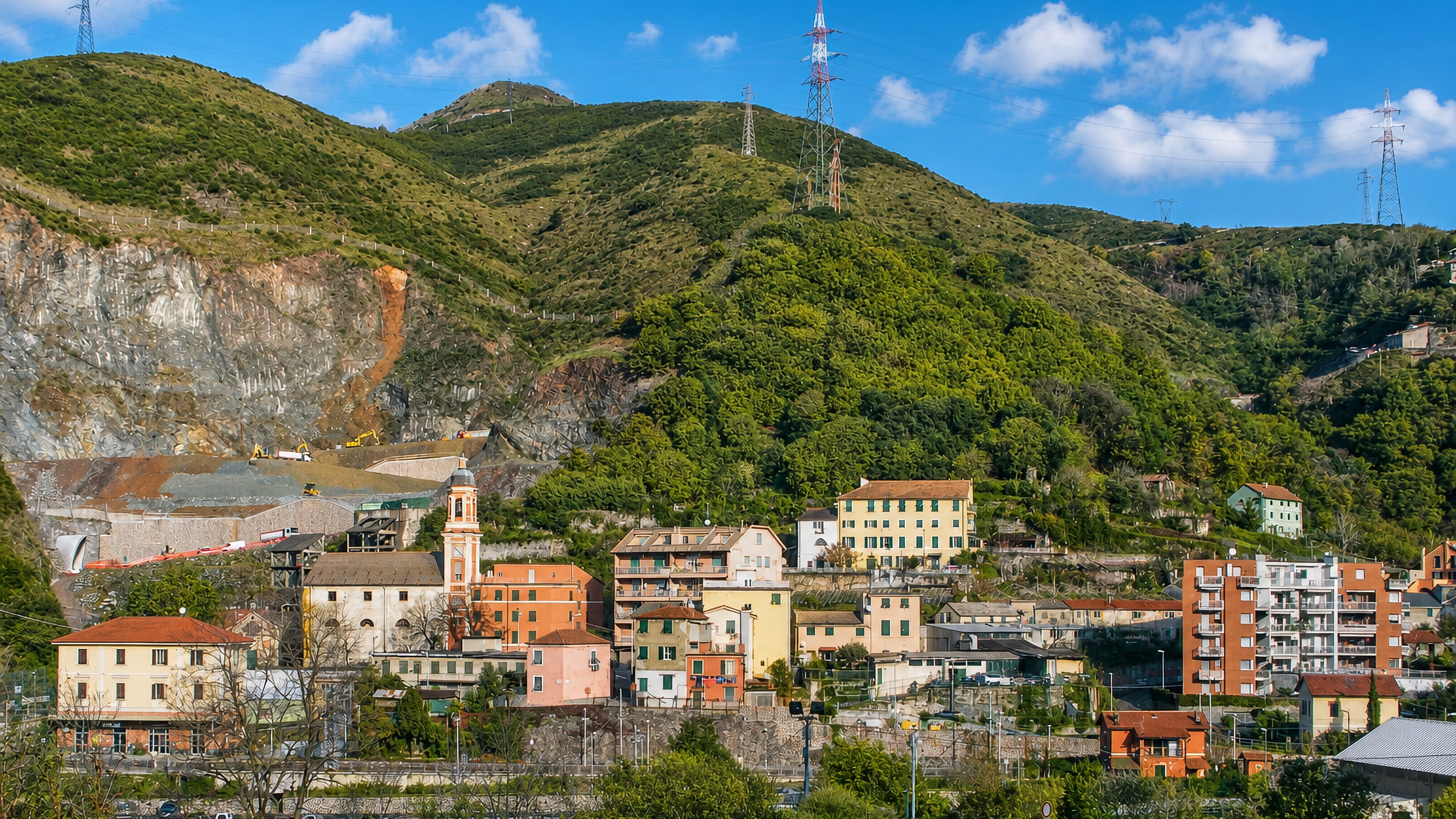 Pastel houses and a church tower on the quarry-scarred hillside of Borzoli in Genoa, Italy.