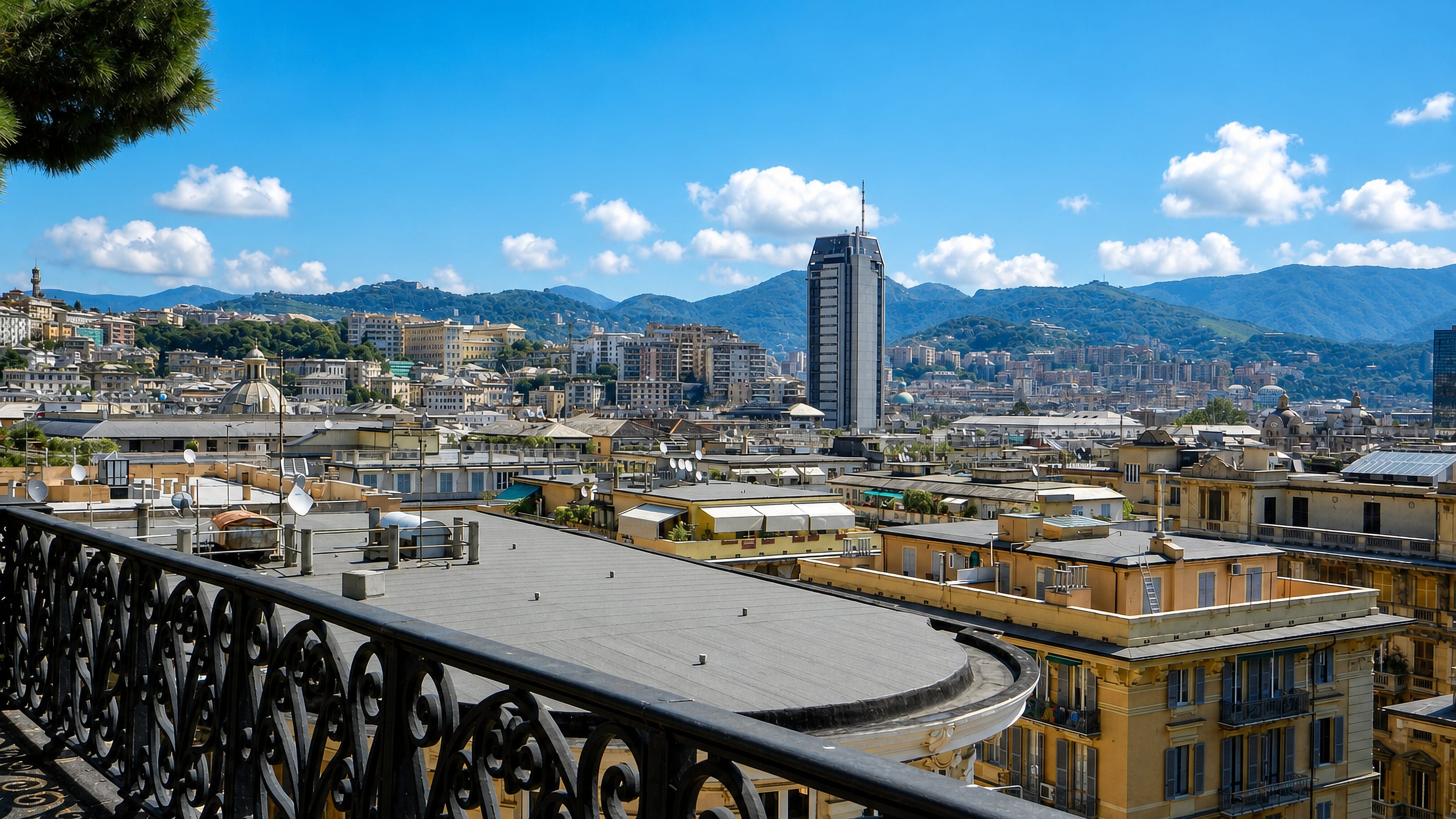 Rooftop view from Carignano over central Genoa, with a glass tower, domes and the Ligurian hills behind.