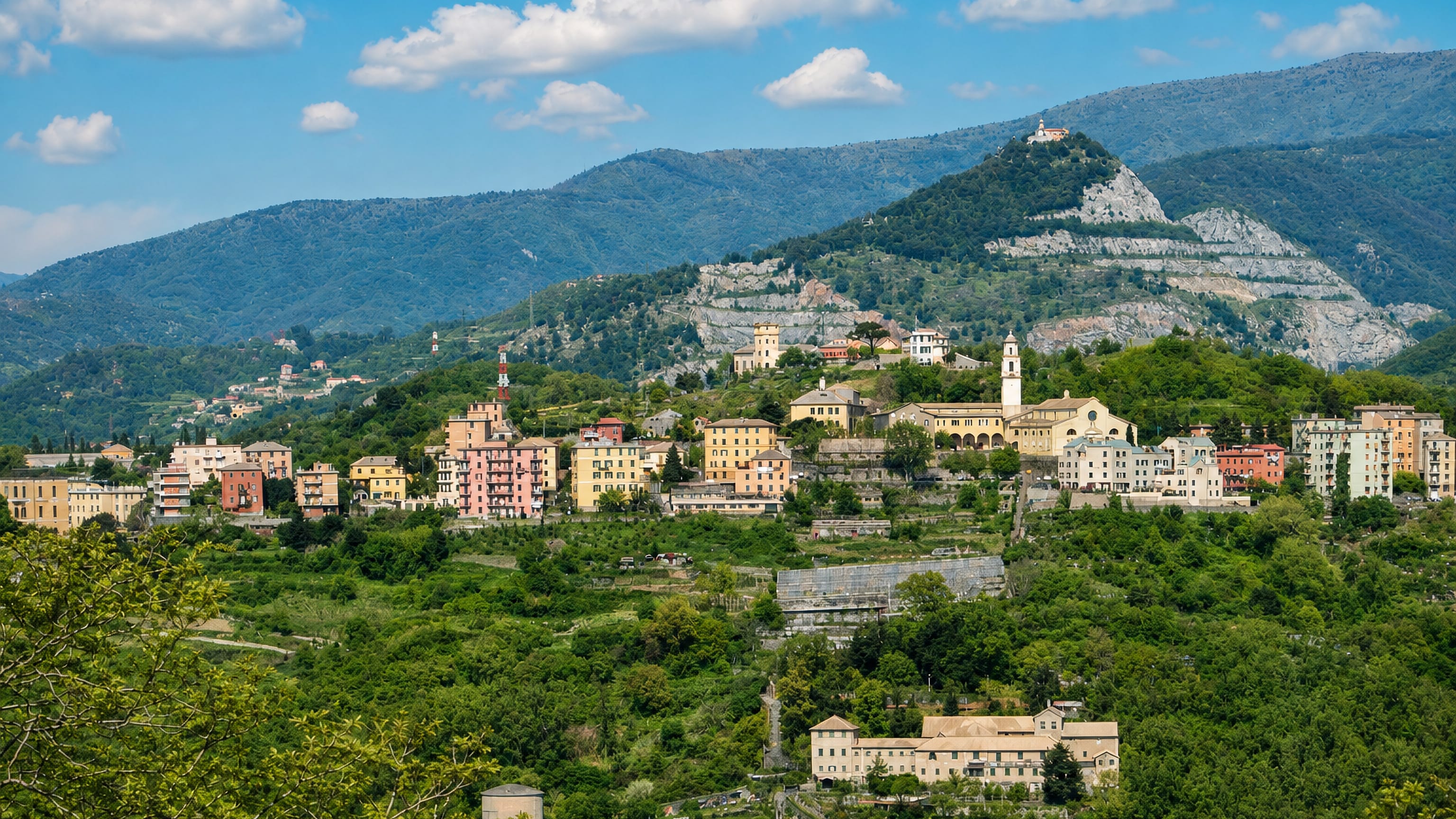 Pastel houses and a church campanile on the terraced hillside of Coronata above Genoa, with mountains behind.