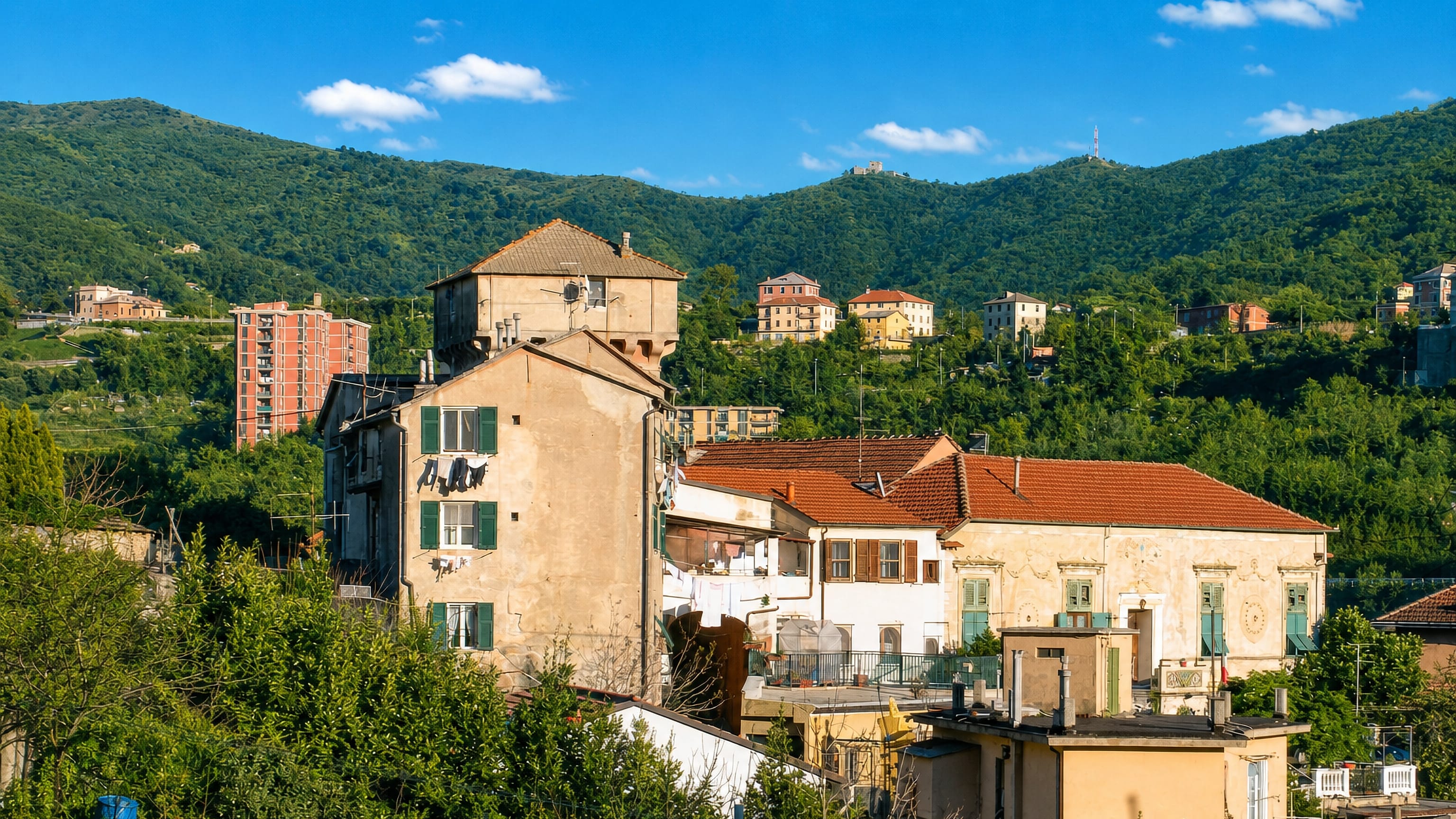 Pastel-plastered houses and a tower block in Fegino below the wooded hills of Genoa's Polcevera valley