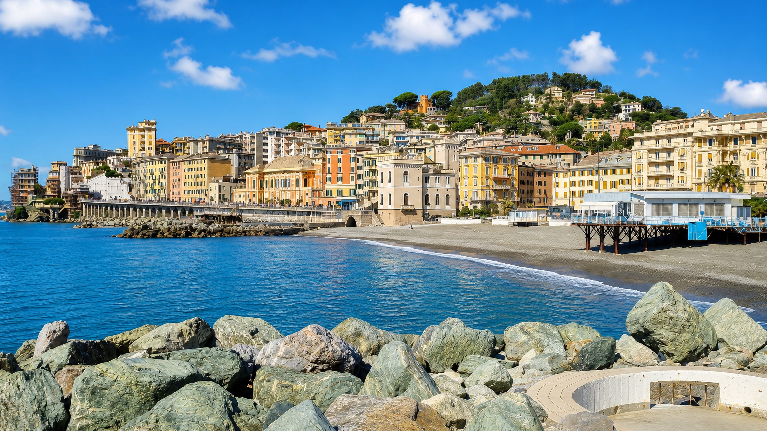 Pastel seafront palazzi, beach and breakwater rocks along the Ligurian shore at Pegli, Genoa.
