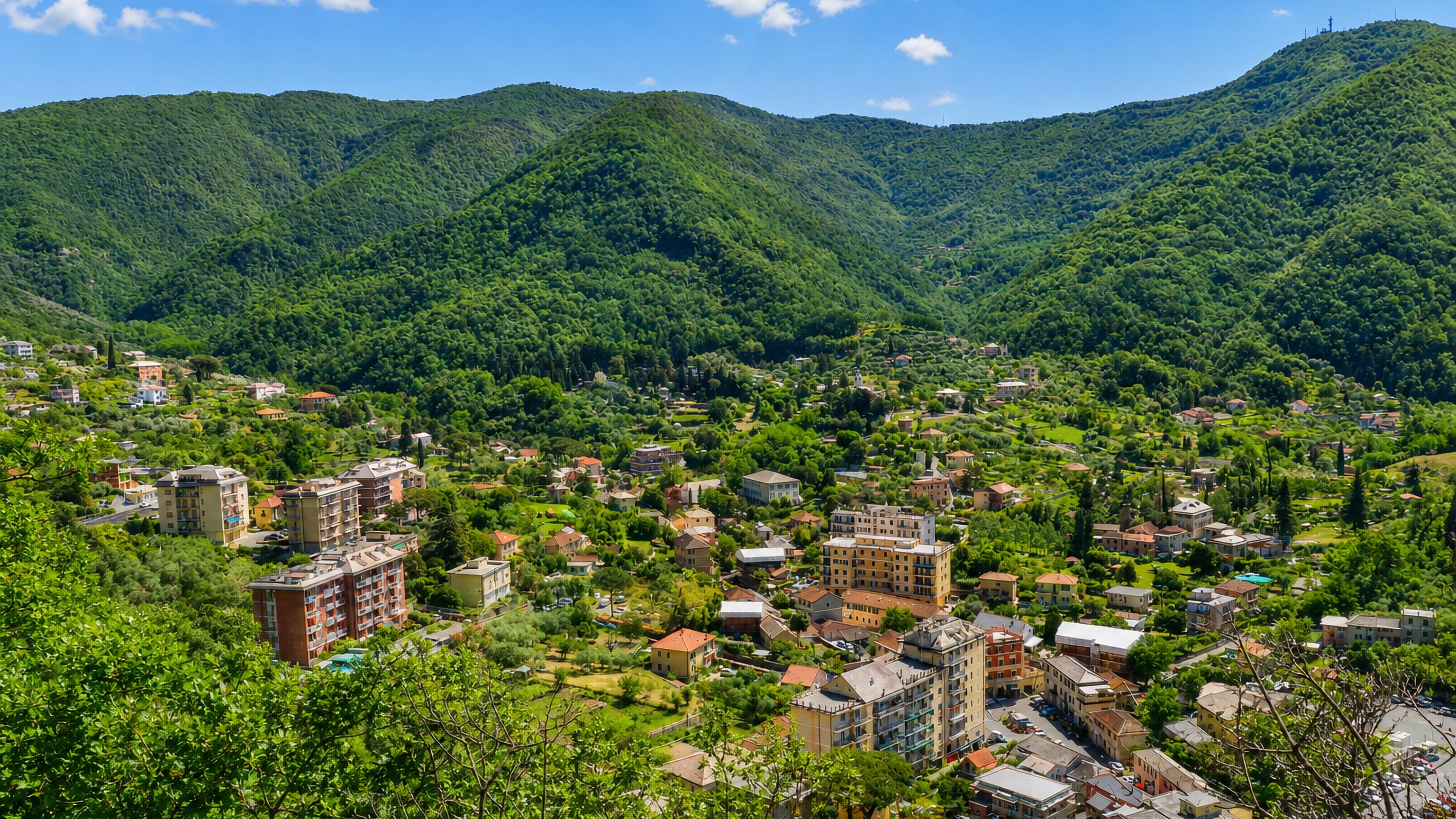 Pastel apartment blocks and houses on the floor of a steep forested valley at San Desiderio, Genoa.