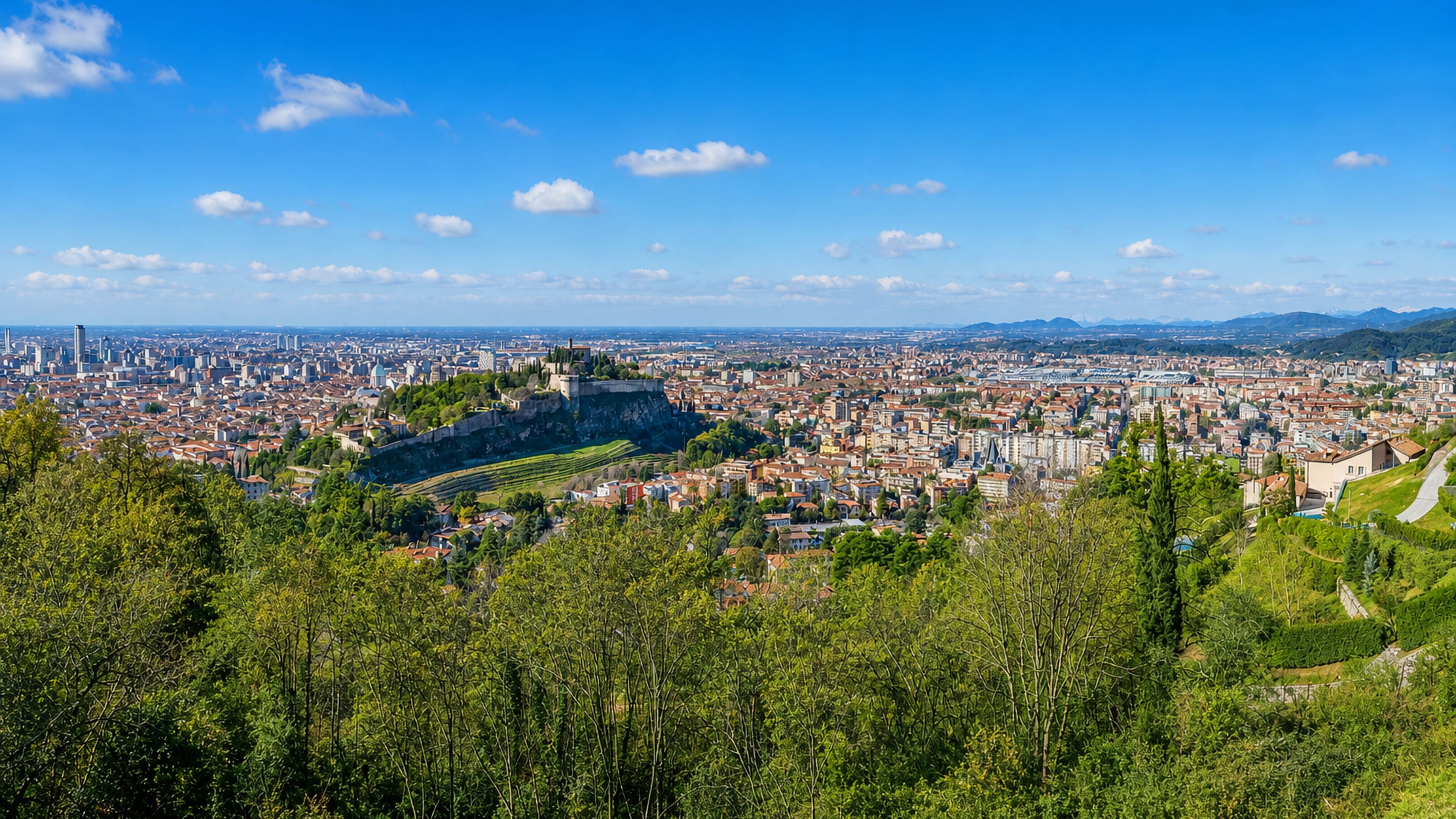 Brescia seen from wooded hills, with the Castello on Cidneo hill and its vineyard above the city's tiled rooftops.