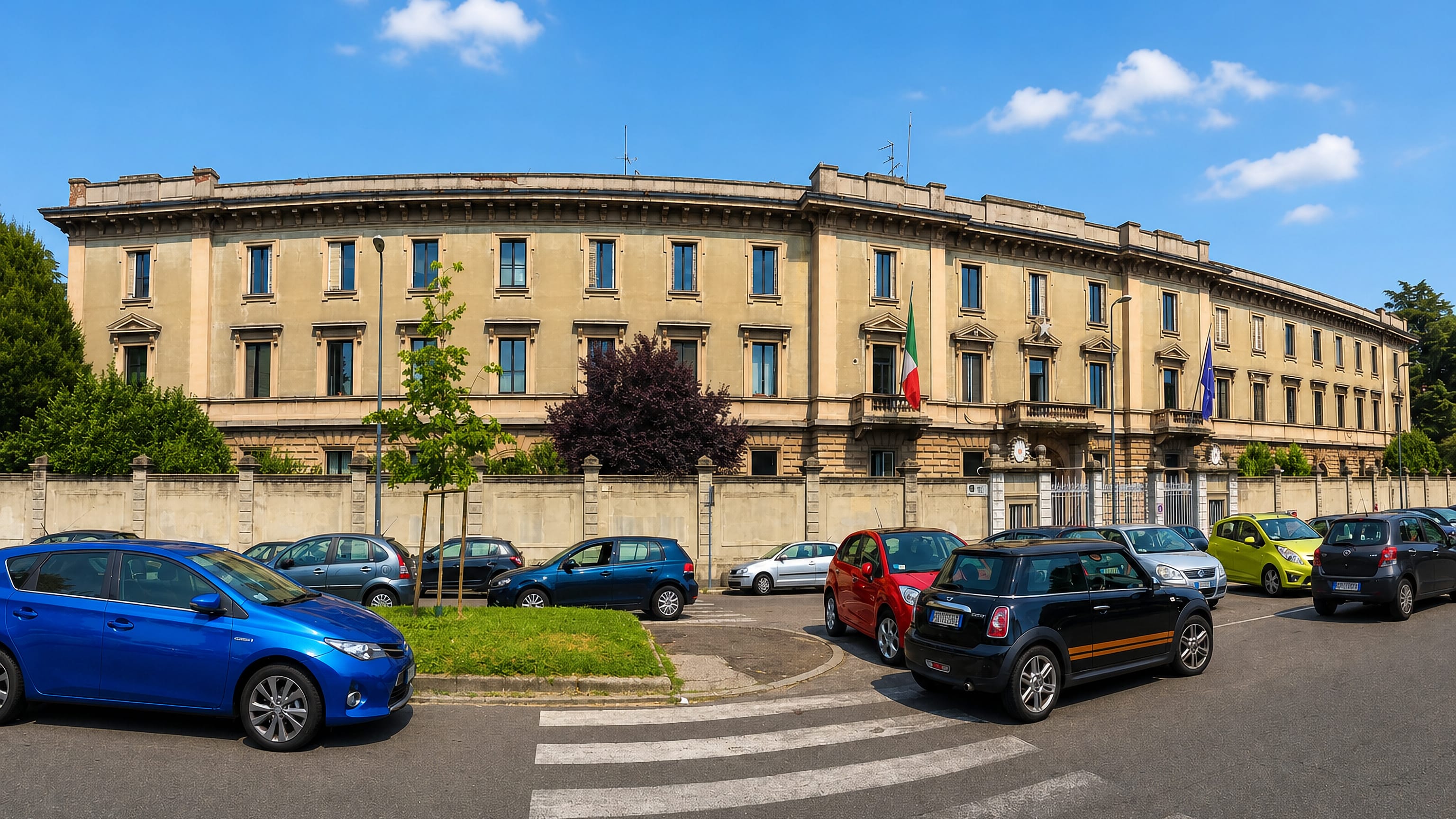 Long neoclassical institutional building flying Italian and EU flags on a street in Baggio, Milan