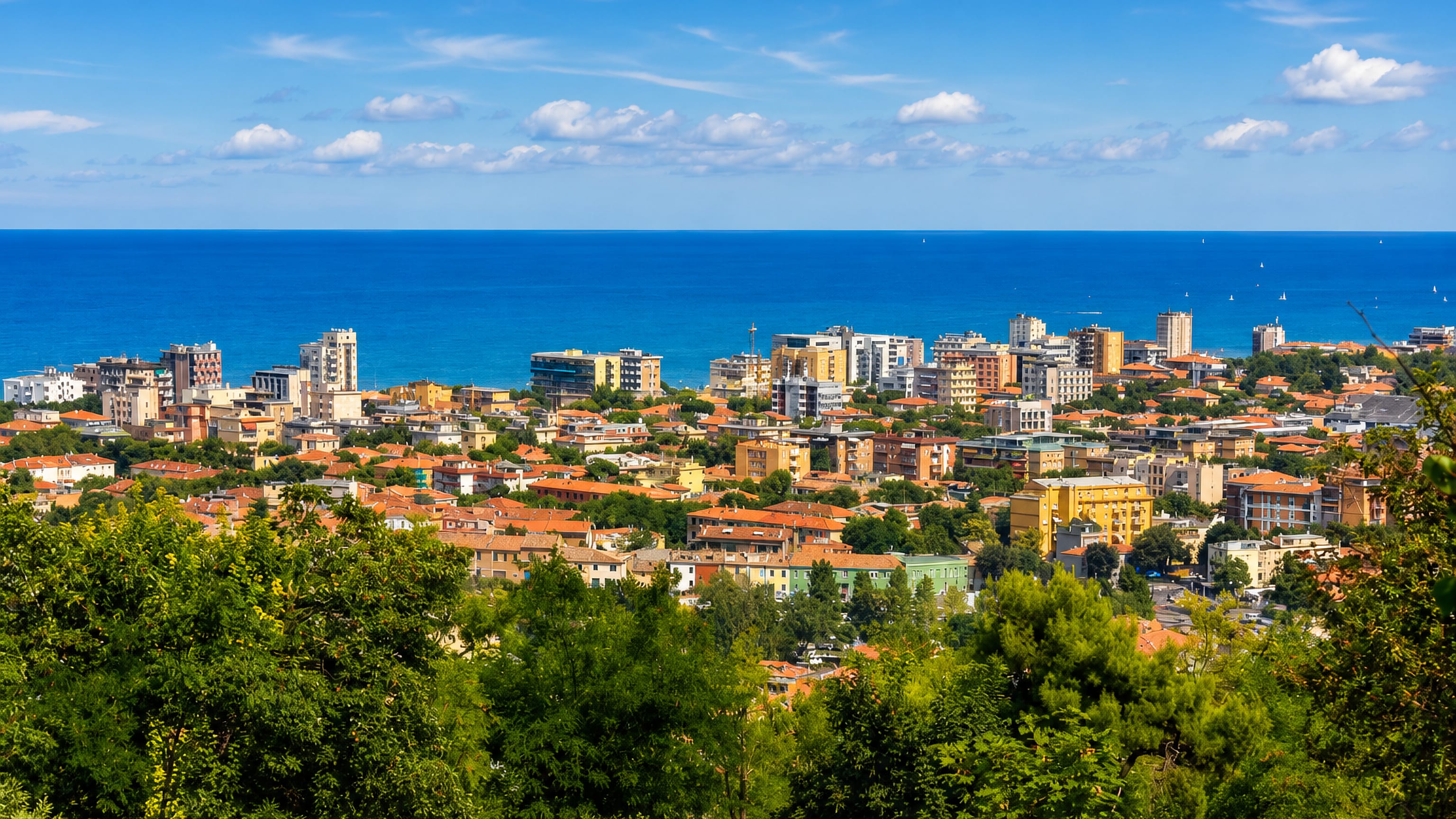 Hilltop view over Pesaro's terracotta rooftops and seafront apartment blocks meeting the blue Adriatic.