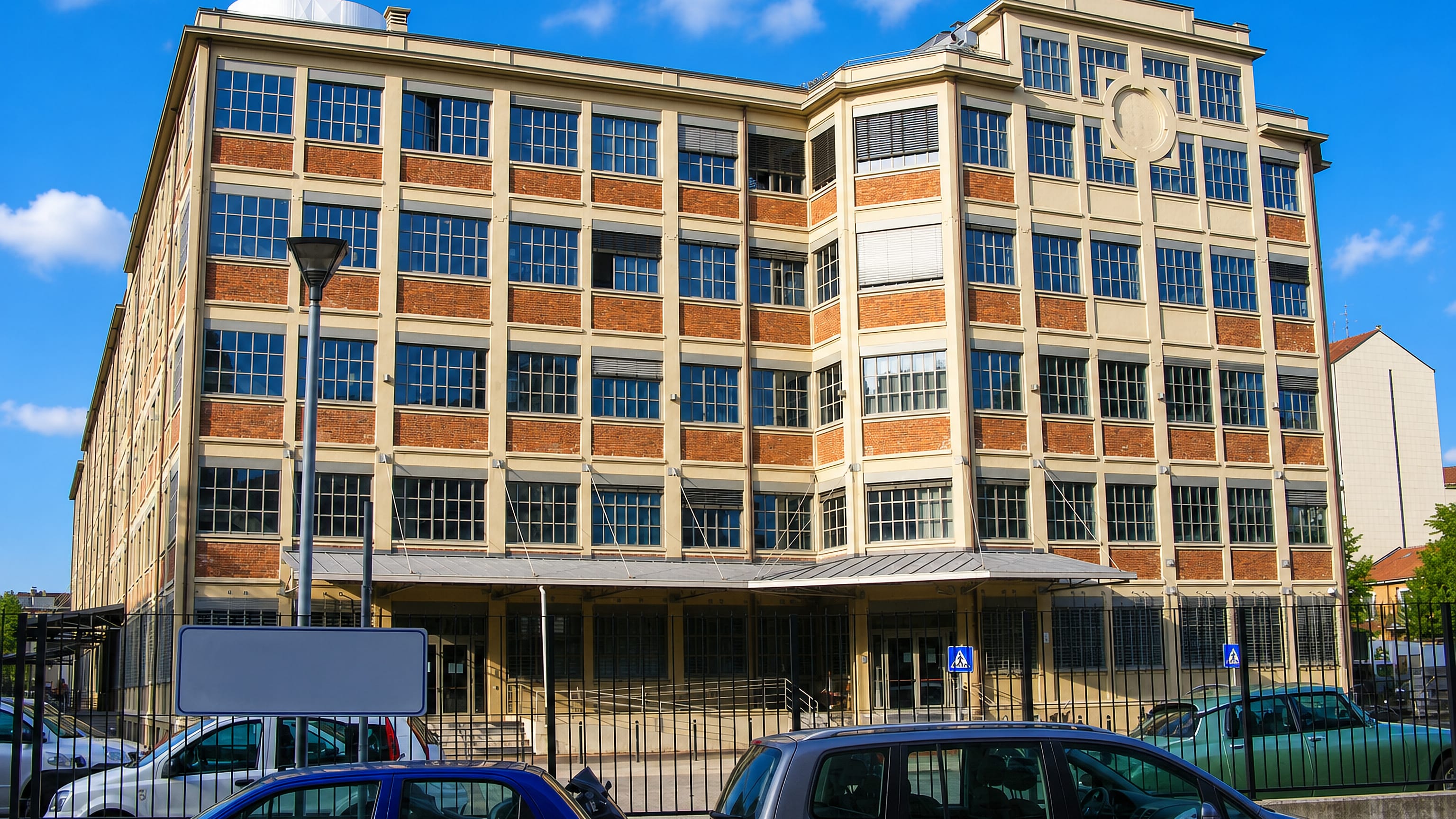 Early 20th-century brick and steel-framed factory building on a sunny street in Cenisia, Turin.