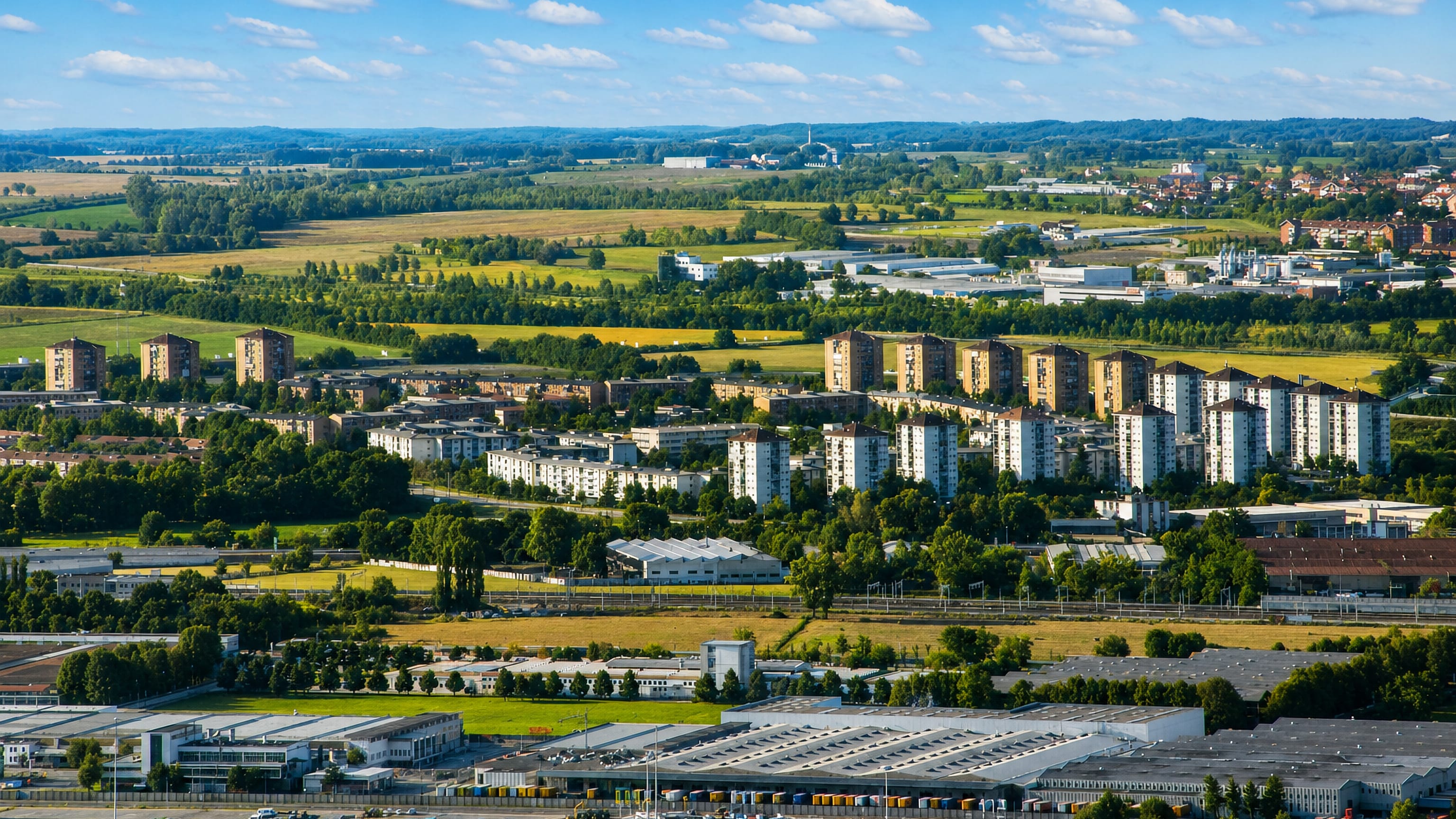 Aerial view of Falchera's housing blocks between fields and industrial sheds on Turin's northern edge.