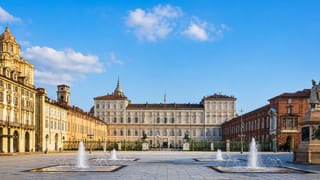 Piazza Castello in Turin with the Royal Palace, its Dioscuri statues and the square's fountains under a clear sky.