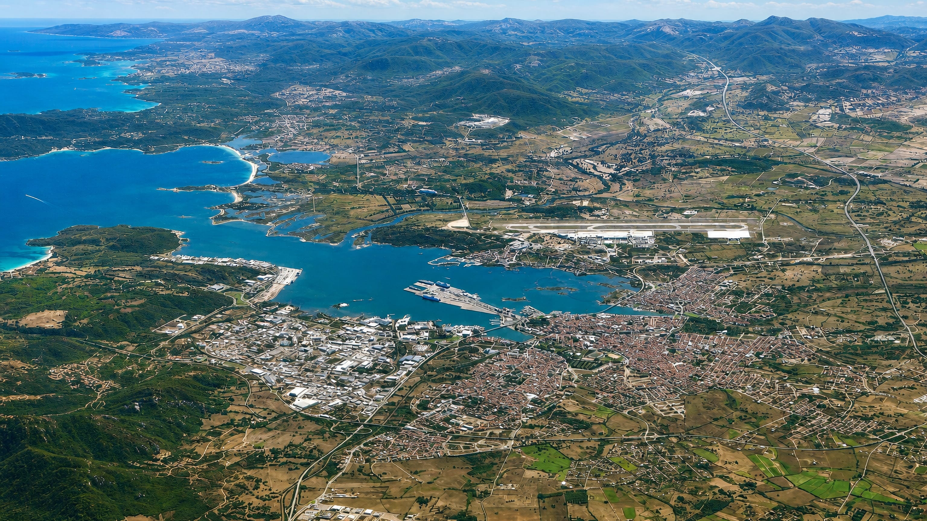 Aerial view over Olbia, Sardinia, with its gulf, ferry port and airport runway ringed by granite hills.