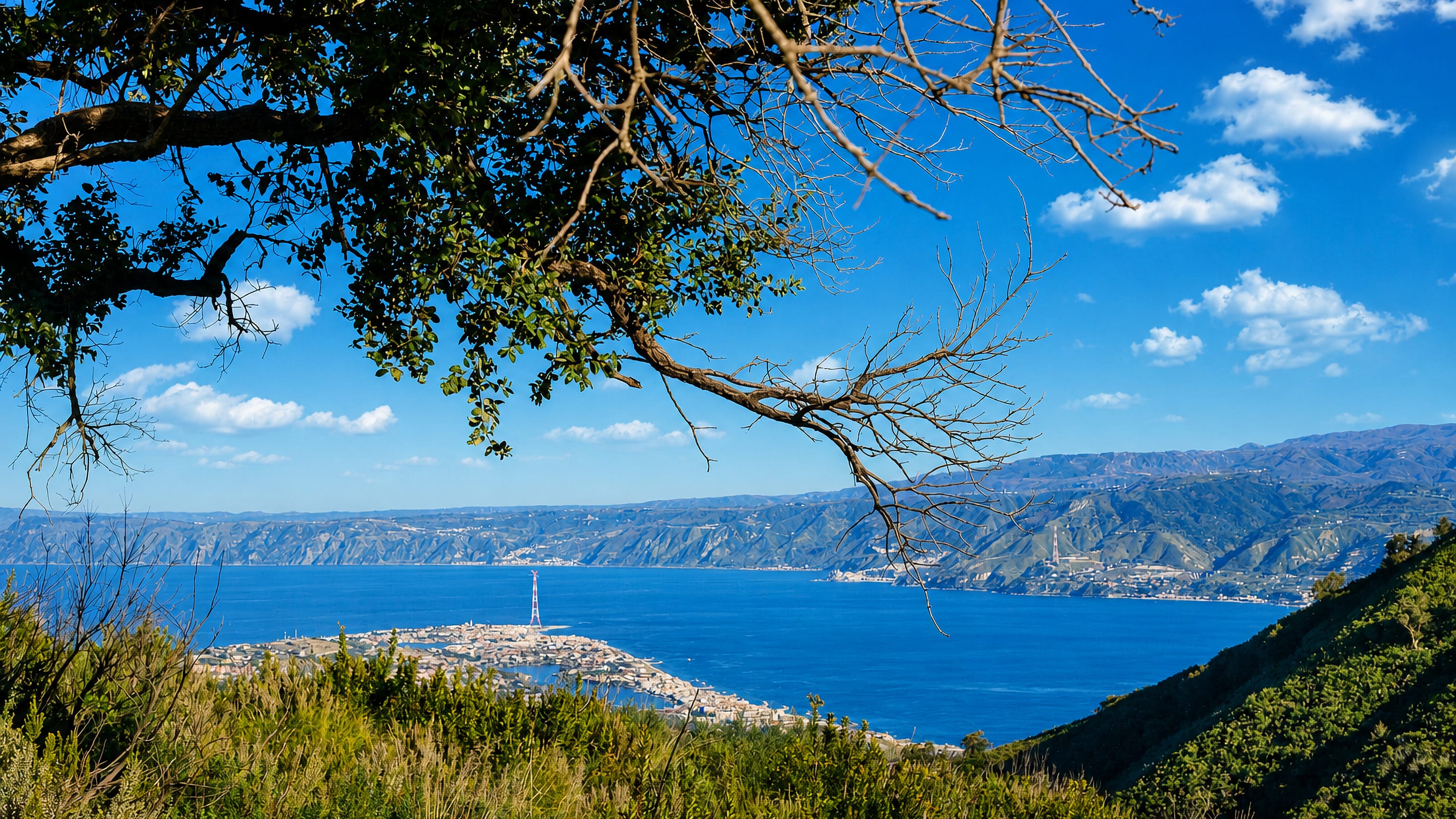 The Strait of Messina seen from a Sicilian hillside, with Torre Faro's pylon and the Calabrian coast beyond